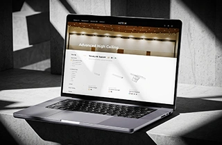 Laptop displaying Meteor Lighting’s “Advanced High Ceiling” webpage with NovaLink System products, set on a modern concrete surface with directional natural light.